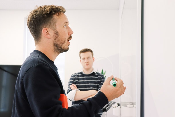 man thinking about strategy and writing on white board with another man watching